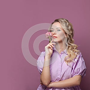 Lovely blonde female model portrait. Perfect woman holding flower on pink background