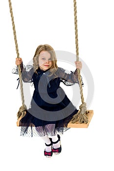 Lovely blonde little girl swinging on rope swing