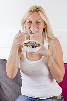 Lovely blonde woman eating cereals with fruit at breakfast