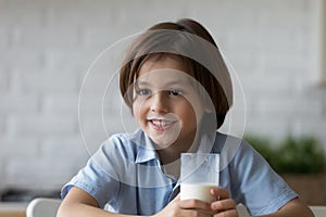 Lovely boy with milk moustaches holds glass of dairy beverage