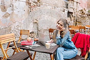 Lovely business woman with long blonde hair using white laptop computer on lunch break at outdoor cafe on brick wall