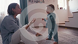 Lovely caucasian baby biy learning to walk taking first step walk to his mother at home. Baby boy walking on the floor
