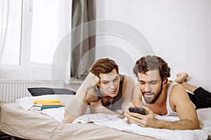 Lovely caucasian gays on bed, use mobile phone