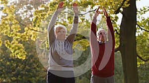 Lovely caucasian heterosexual couple of pensioner seniors exercising, stretching in park, taking care of their physical