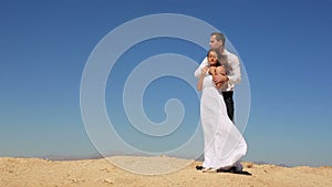 Lovely cheerful couple of newlyweds is tenderly hugging on the sand beach over the blue sky in Egypt.