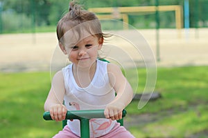 Lovely cheerful little girl kindergartner in a T-shirt rides on a swing in the park against the background of the playground photo