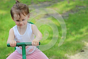 Lovely cheerful little girl kindergartner in a T-shirt rides on a swing on a playground against a background of green grass photo