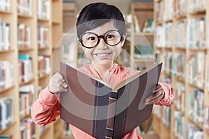 Lovely child with glasses holding book in library