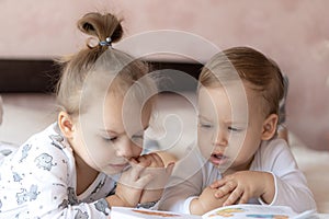 Lovely children - brother and sister, reading a book, on the bed. Close up of children in bed reading a book. A boy and