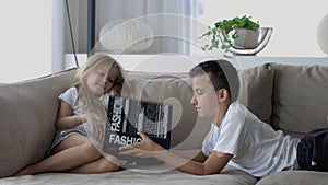 Lovely children brother and sister, reading a book, on the sofa