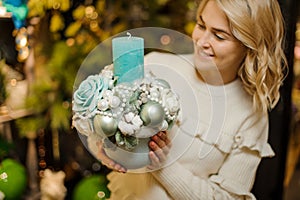 Lovely christmas composition of balls in pot with candle in hands of blonde woman