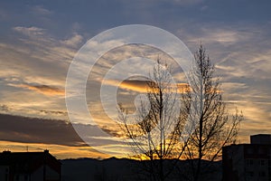 Krásné mraky nad městem a domy nebo parkem a loukou, při východu nebo západu slunce.