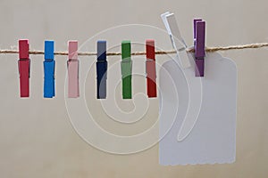 The lovely colorful cloths pins and a white tag label hanging on the brown string with the wall background