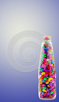 Lovely colorful small pebbles with pink, blue, green, grey and white pebbles in a clear glass bottle with a blue shaded background