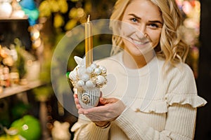 Lovely composition in pot of white Christmas balls and golden candle in hands of woman