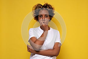 Lovely confused african woman with curly hair against yellow wall.