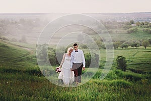 Lovely couple, bride and groom posing in field during sunset, lifestyle