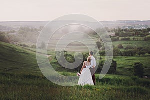 Lovely couple, bride and groom posing in field during sunset, lifestyle