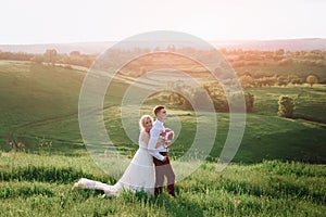 Lovely couple, bride and groom posing in field during sunset, lifestyle