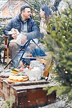 Lovely couple with cute dog sitting on backyard outside surrounded by young coniferous trees