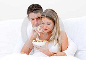 Lovely couple eating fruit salad in bed