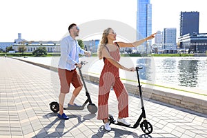 Lovely couple having fun driving electric scooter along the city promenade