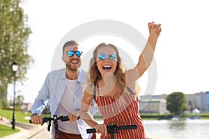 Lovely couple having fun driving electric scooter along the city promenade