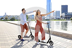 Lovely couple having fun driving electric scooter along the city promenade