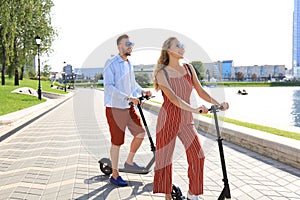 Lovely couple having fun driving electric scooter along the city promenade