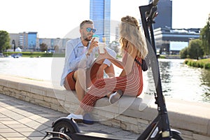 Lovely couple having fun driving electric scooter through the city, having a break, drinking coffee