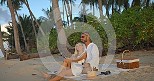 Lovely couple having picnic on evening sandy beach man hugs his girlfriend, enjoying time together