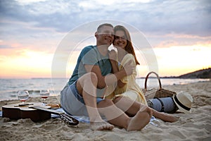 Lovely couple having romantic picnic on beach at sunset