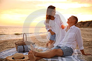 Lovely couple having romantic picnic on beach at sunset