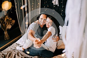 Lovely couple hugging on their bed decorated with garland lights at home indoors in the bedroom