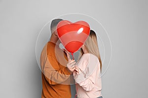 Lovely couple kissing behind heart shaped balloon on grey background. Valentine`s day celebration