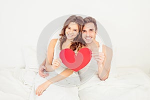 Lovely couple in love holding red paper heart in bed