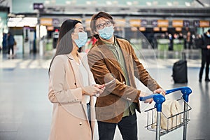 Lovely couple in medical masks walking down airport terminal