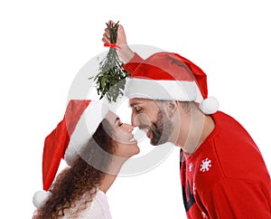 Lovely couple in Santa hats under mistletoe bunch on white background