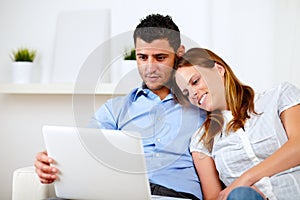 Lovely couple smiling and reading on laptop