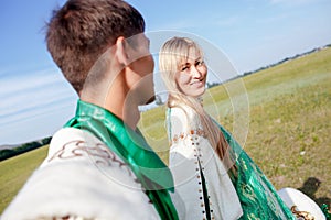 Lovely couple in traditional attire walking outdoors at sunny summer day, stage costume.