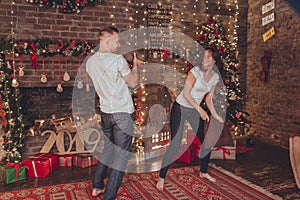 Lovely couple woman and man are fighting with pillows at home near fireplace. Christmas time.