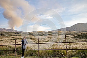 Lovely cute japanese girl standing on Aso active volcano background with smoke at Mount Aso Nakadake, Kumamoto