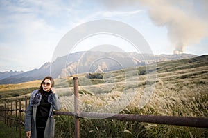 Lovely cute japanese girl standing on Aso active volcano background with smoke at Mount Aso Nakadake, Kumamoto