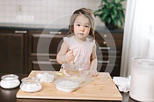 Lovely cute little girl wearing white dress is whisking eggs in mixing bowl with fork