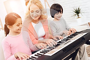 Lovely elderly woman teaches small grandchildren to play synthesizer.
