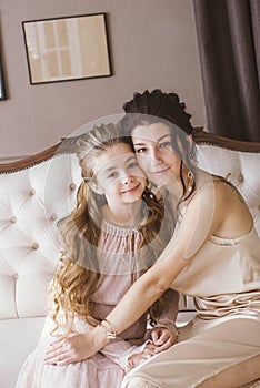 Lovely and elegant mother and daughter, in beautiful fashionable dresses with hairstyles in a classic light interior.