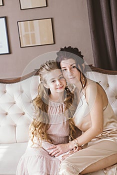 Lovely and elegant mother and daughter, in beautiful fashionable dresses with hairstyles in a classic light interior.