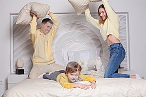 Lovely family, mom and dad with adorable child son playing with pillows on the bed