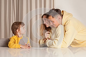 Lovely family, mom and dad in yellow clothes with their child son sitting by the table and having fun