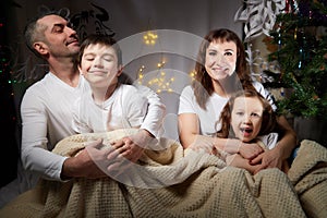 Lovely Family with mother, father, son and daughter having fun in room derorated fot Christmas night. Children and
